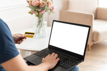 Man is holding a credit card and using laptop computer with blank screen at home. Online shopping...