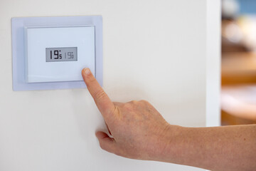 Person adjusting the temperature of their thermostat - 695295616