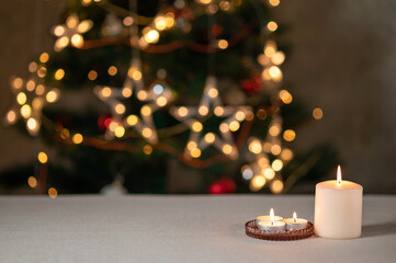 Candles on empty beige table, defocused Christmas tree with sparkling garland lights on background,...