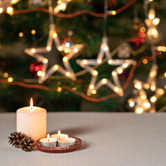 Festive Christmas holiday background, candle lights and pine cones on beige table, blurred sparkling star shape garland lights decoration on Christmas tree
