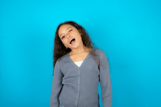 Beautiful teen gil wearing casaul clothes over blue background winking looking at the camera with sexy expression, cheerful and happy face.