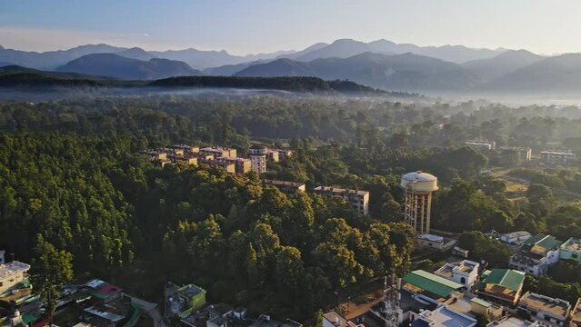 An aerial view of Dehradun, an Indian city during sunrise or sunset, with cloudy weather and rows of residential houses surrounded with greenery. The Himalayan city is surrounded by rainforest.