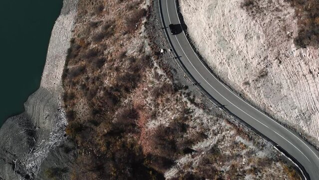 a dark car drives along a serpentine road in Georgia, top view. a black car drives along the road near the water. view from a drone, from above, following. Zhinvali