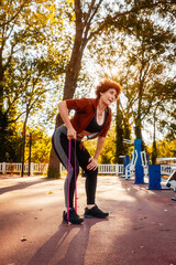 Adult Caucasian woman does stretching with elastic band on street. Healthy lifestyle and training in park. Vertical orientation - obrazy, fototapety, plakaty