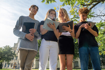 Focused young students take notes while standing in front of campus. Group of students listens to...