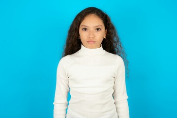 Offended dissatisfied Beautiful kid girl standing over blue background with moody displeased...