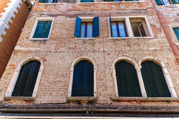 Old town of City of Venice with weathered facades and closed wooden shutters on a blue cloudy summer day. Photo taken August 6th, 2023, Venice, Italy.