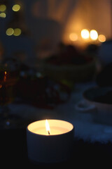 Cup of tea or coffee, glass of wine or juice, bowl of cookies, organic pomegranate, fluffy blanket, pine cones, various Christmas decorations and lit candles on the table. Christmas hygge concept.