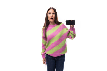pretty young european brunette woman dressed in striped pink pullover showing horizontal phone screen on white background with copy space