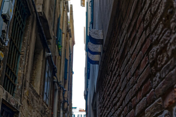Narrow alley at the old town of Venice with brick wall facades of historic houses on a sunny summer day. Photo taken August 6th, 2023, Venice, Italy.