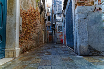 Diminishing perspective of narrow alley at the old town of Venice with facades of historic houses on a sunny summer day. Photo taken August 6th, 2023, Venice, Italy.