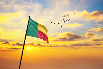 Waving flag of Benin against the background of a sunset or sunrise. Benin flag for Independence...