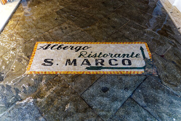 Mosaic direction sign on the floor flooded by high tide of restaurant named San Marco at the old town of Venice on a cloudy summer day. Photo taken August 6th, 2023, Venice, Italy.