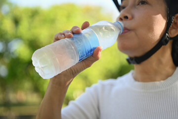 Senior fitness woman drinking water from a bottle resting after riding bicycle in park.