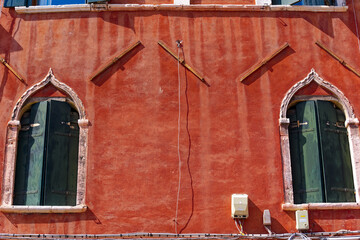 Scenic view of cityscape with close-up of red facade of historic house with green wooden shutters at City of Venice on a sunny summer day. Photo taken August 6th, 2023, Venice, Italy.