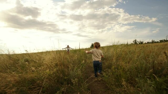 Mom plays with her little daughter in a field at sunset. The girl rejoices and smiles. A pretty young woman and her little daughter are spending time on a warm, summer evening.