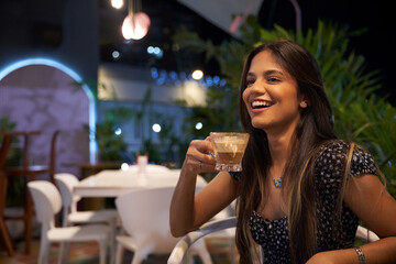 Mujer Joven latina  de cabello castaño largo tomando cafe sentada 