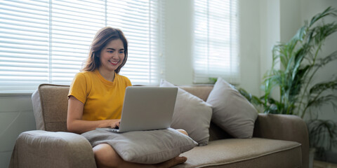 Young woman Asian using laptop pc computer on couch relax surfing the internet at home. lifestyle...
