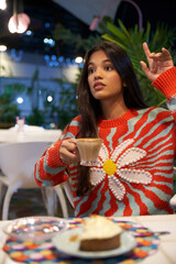 Mujer Joven latina  de cabello castaño largo tomando cafe sentada llamando a camarera