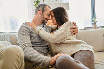 cheerful child-free couple smiling face to face with closed eyes in living room at home, serenity