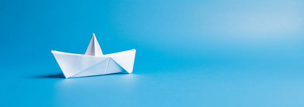 Creative image of white origami ships placed behind blue and orange paper ship representing concept of leadership on light background Copy space. Business concept design.