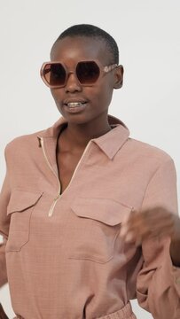 Young happy bold African American female model in stylish pink clothes standing looking at camera over sunglasses against white background
