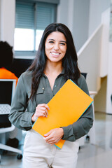 Woman holding a folder and smiling while posing standing in the office. Business concept.