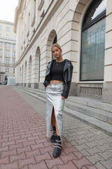 Fashion street beauty woman in casual urban outfit with leather jacket and skirt with boots in the city near a vintage building