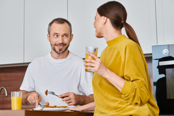 smiling man having delicious breakfast near wife with orange juice in kitchen, child-free lifestyle