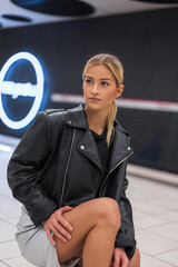 Fashionable beautiful fresh urban woman in stylish clothes with leather jacket sitting and posing at metro station