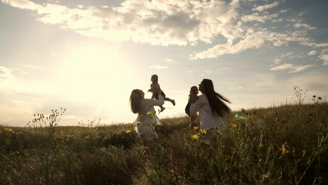 Happy family at sunset in a field. Silhouette of a group of people walking across a field. Happy child with parents holding hands. Concept of happy family, clothing advertising and family vacation