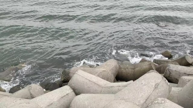 Sea water splashing after waves hitting on tetrapod a massive triangle shape concrete stone structure near beach or sea shore used to protect land from heavy ocean tidal waves. Closeup aerial view.