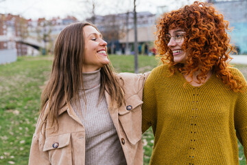 Joyful redhead and brunette women laughing together in a park setting