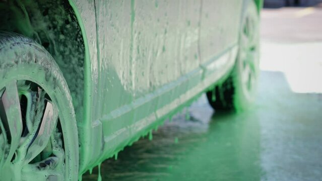 Cropped image of the wheel of a car in an outdoor self-service car wash, covered with cleaning soap foam.