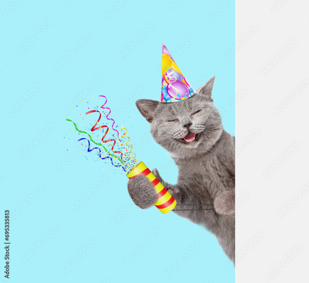 Aufkleber Smiling cat wearing party cap holds exploding firecracker and looks from behind empty white banner. Isolated on blue background