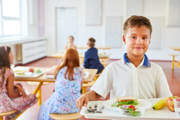 Boy holding tray with healthy meal in school cafe