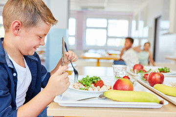 Happy boy eating meal with cutlery in school cafeteria