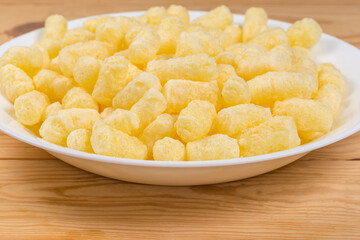 Sweet corn puffs on white plate, side view close-up