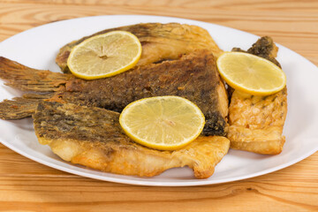Fried carp pieces on dish, side view on rustic table