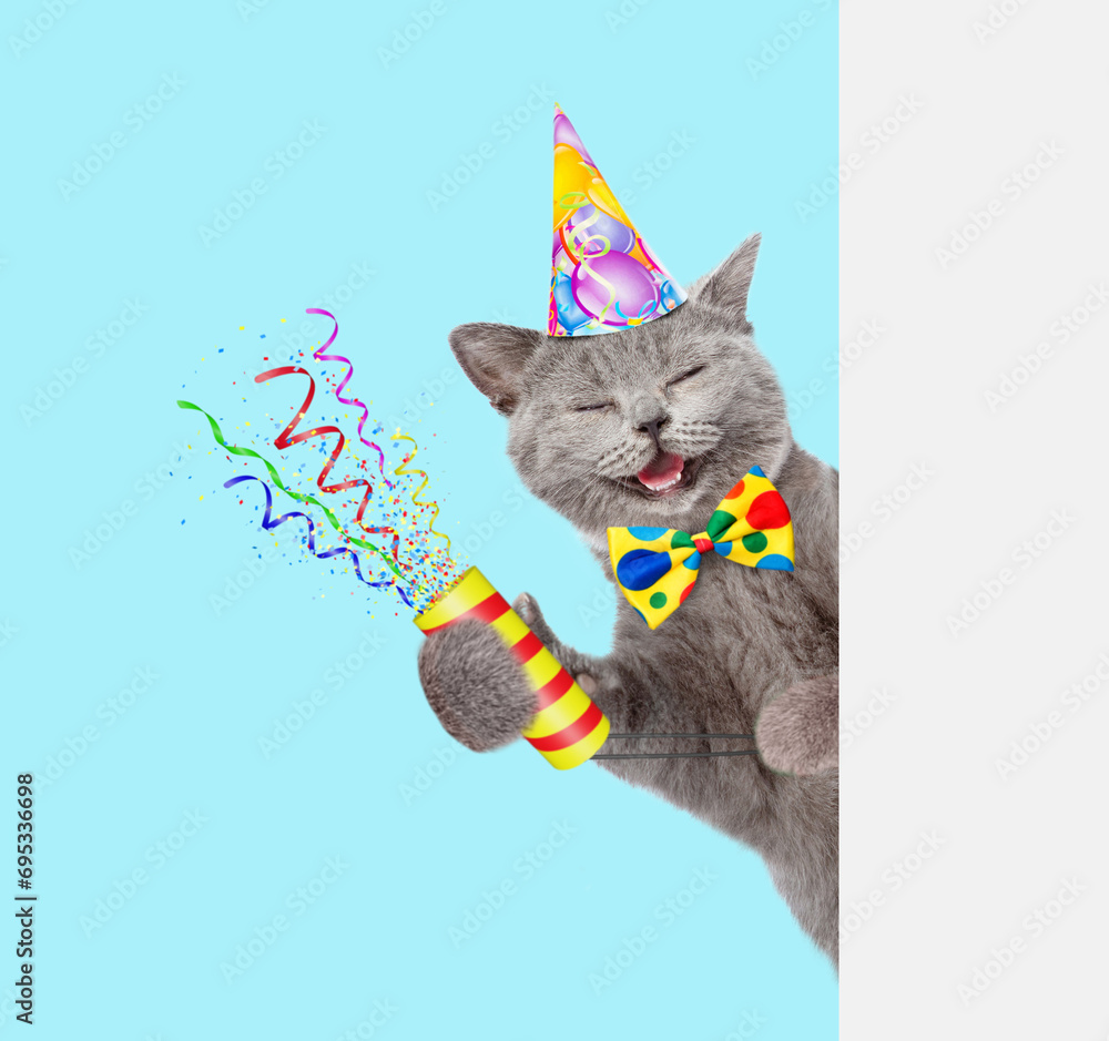 Aufkleber Happy cat wearing party cap holds exploding firecracker and looks from behind empty white banner. Isolated on blue background