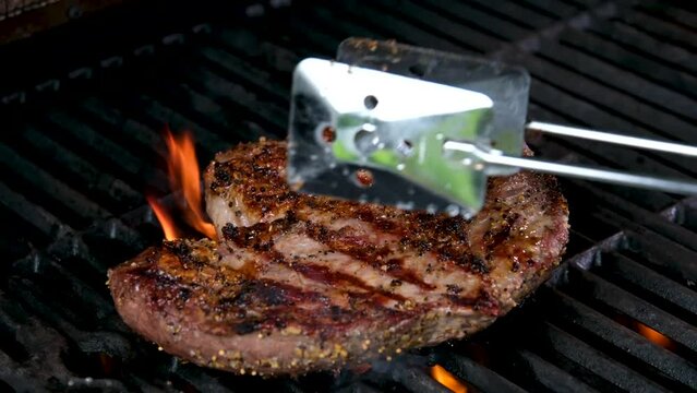 Grilled meat steak on stainless grill depot with flames on dark background. Food and cuisine concept.