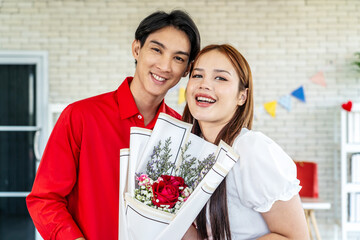 Young asian woman receives a bouquet of red roses as a gift from a man or boyfriend. Portrait of a young woman in the living room with a bouquet of flowers. Anniversary, Women's Day, Valentine's Day.
