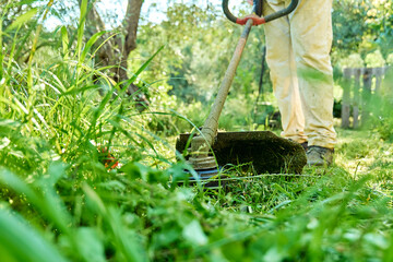 Gardener mowing weeds in the garden with string grass trimmer. Man using lawnmower in yard, cutting...