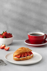 A fresh croissant with ricotta and fresh strawberries. Croissant with black coffee.