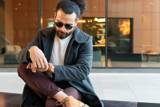 Stylish man sitting and checking his watch in the city