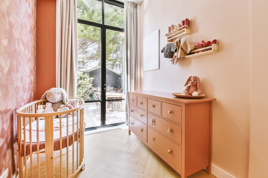 Pink nursery with crib and dresser by bright window