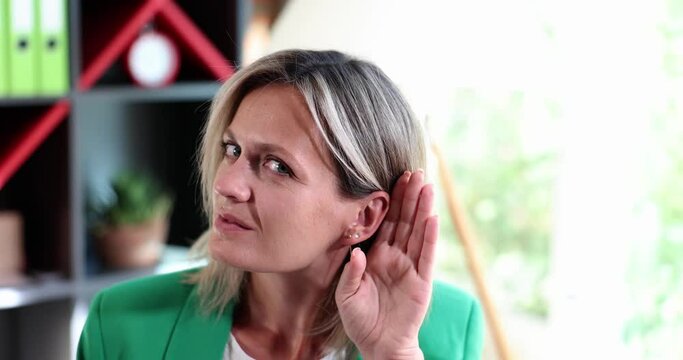 Portrait of curious sly lady eavesdropping with palm of ear in office. Trade secret protection business secrets
