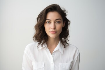 Fototapeta premium Portrait of a content woman in her 20s wearing a classic white shirt against a white background. AI Generation