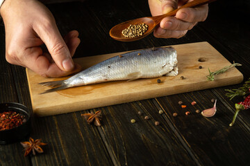 The cook preparing Atlantic herring fish on the kitchen table with spices and coriander for a...