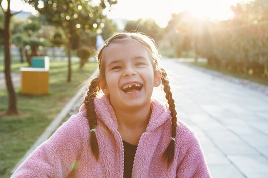 portrait of a laughing funny cheerful girl 6 years old in the park at sunset, missing front tooth.